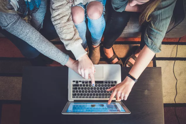 Tre personers ben vid en uppfälld laptop