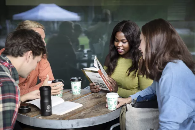 Tre personer sitter kring ett bord och diskuterar. en person håller i en bok.