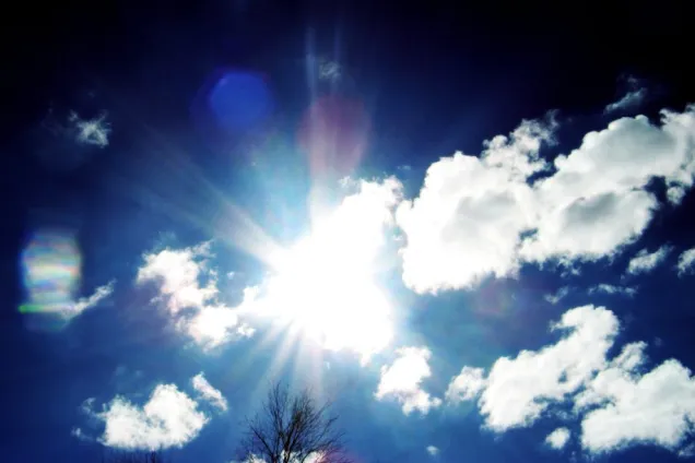 En blå himmel med sol och några vita moln.